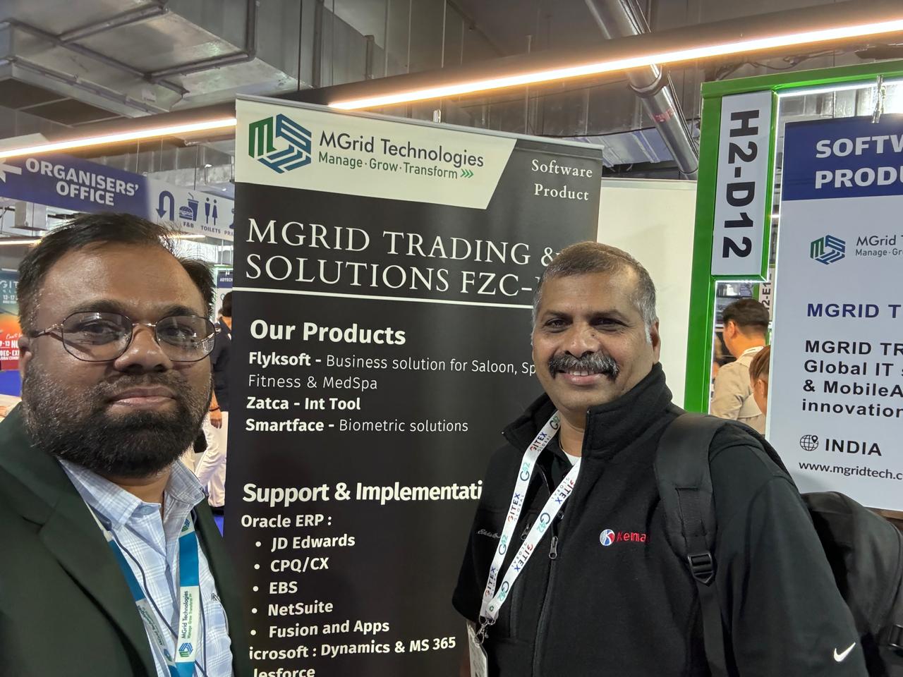 Two visitors beside the MGrid Technologies stand banner at GITEX Global 2025